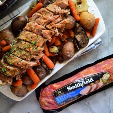 Plated Pork Tenderloin on bed of carrots and potatoes next to package of Smithfield.