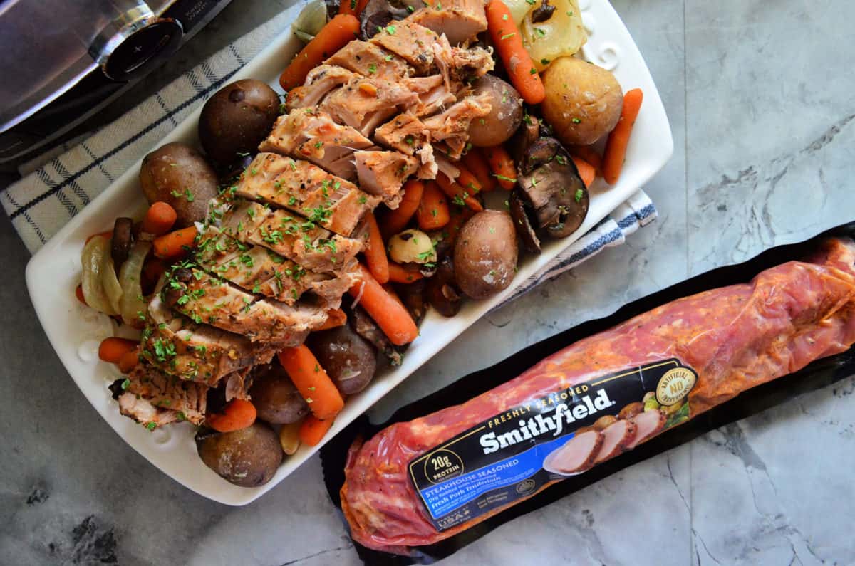 tenderloin sliced on platter over potatoes, onions, carrots, garlic, and carrots next to smithfield packaging.