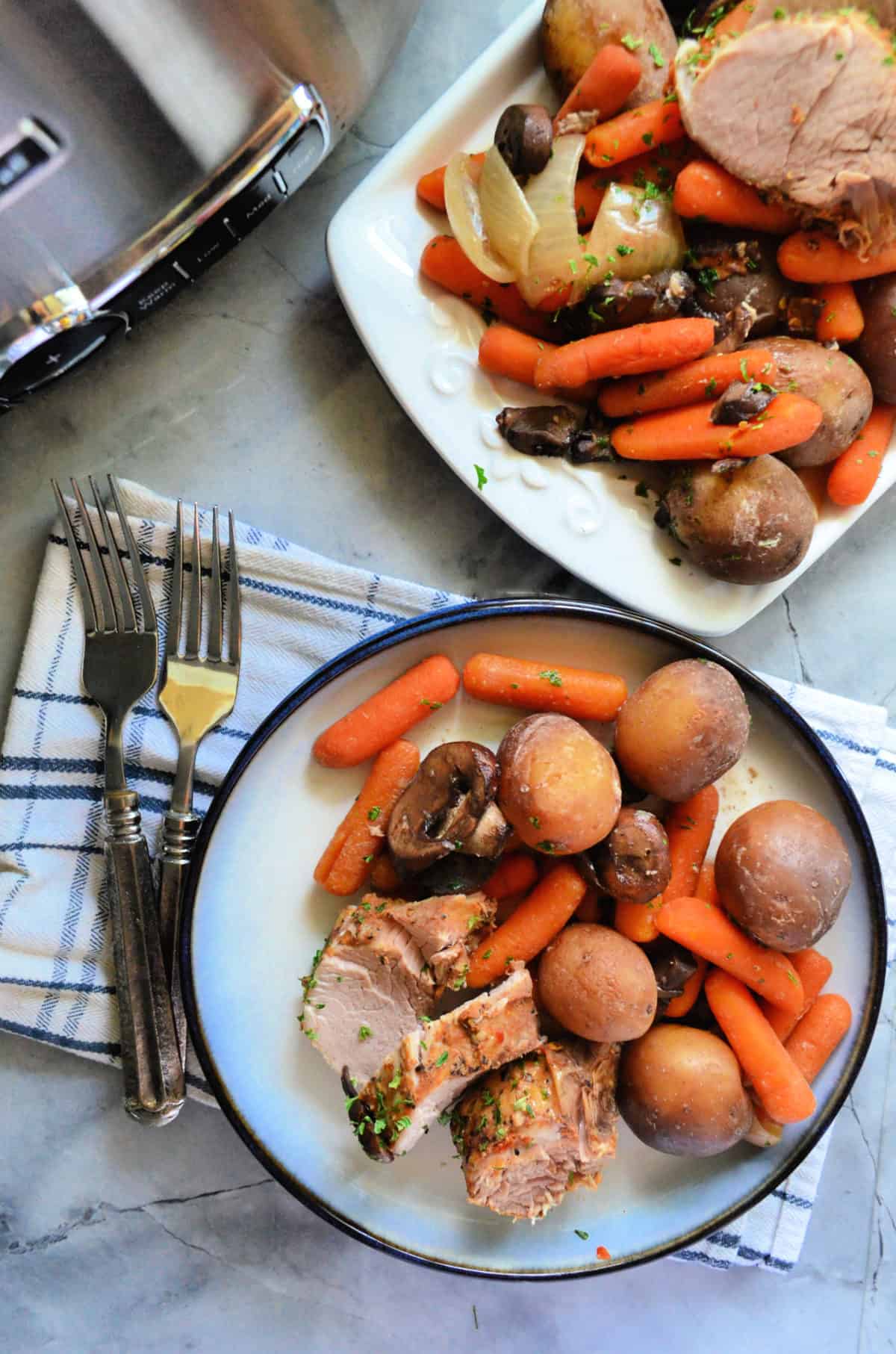 Plated sliced tenderloin, carrots, mushrooms, and potatoes with fork next to platter of remnants.