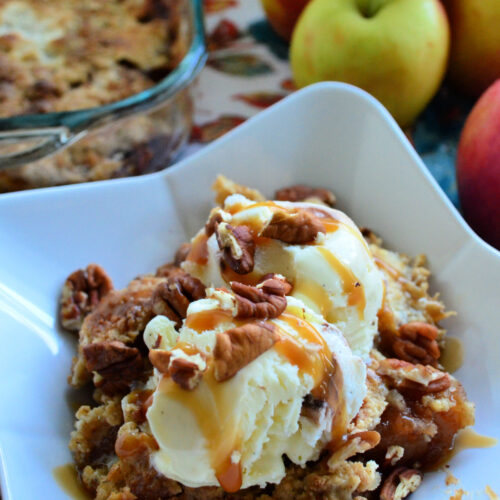 Close up Apple Dump Cake topped with vanilla ice cream, pecans, and caramel drizzle.
