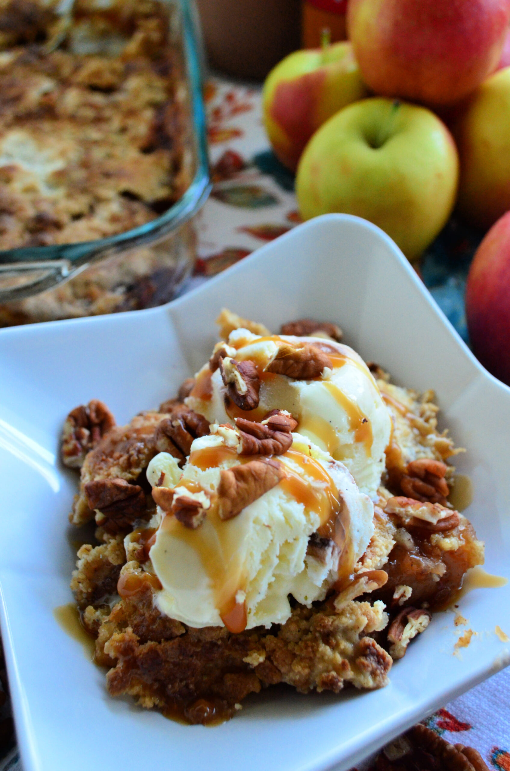 Close up Apple Dump Cake topped with vanilla ice cream, pecans, and caramel drizzle.