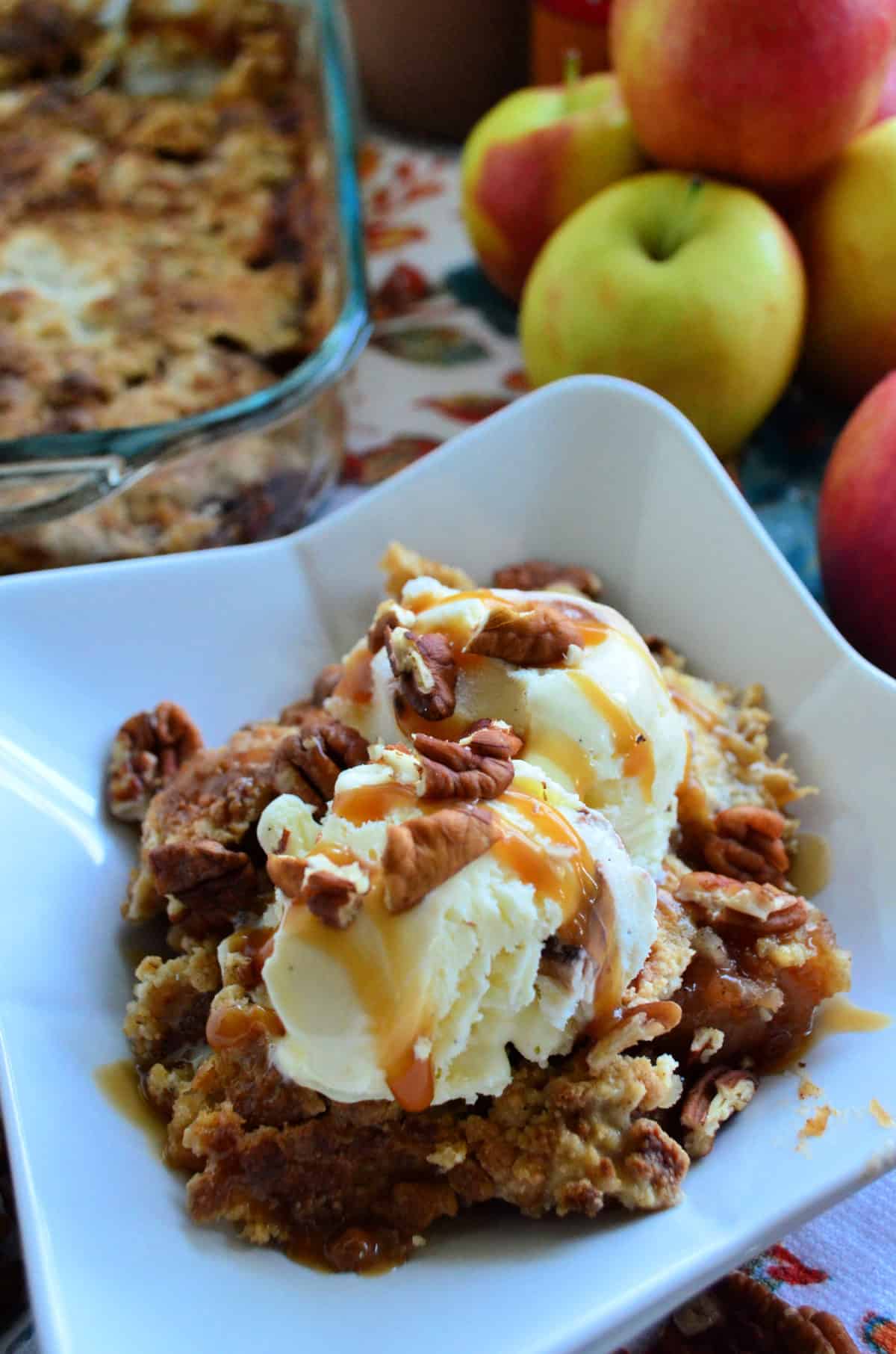 closeup of crumbled looking light brown cake with pecans topped with ice cream and caramel.