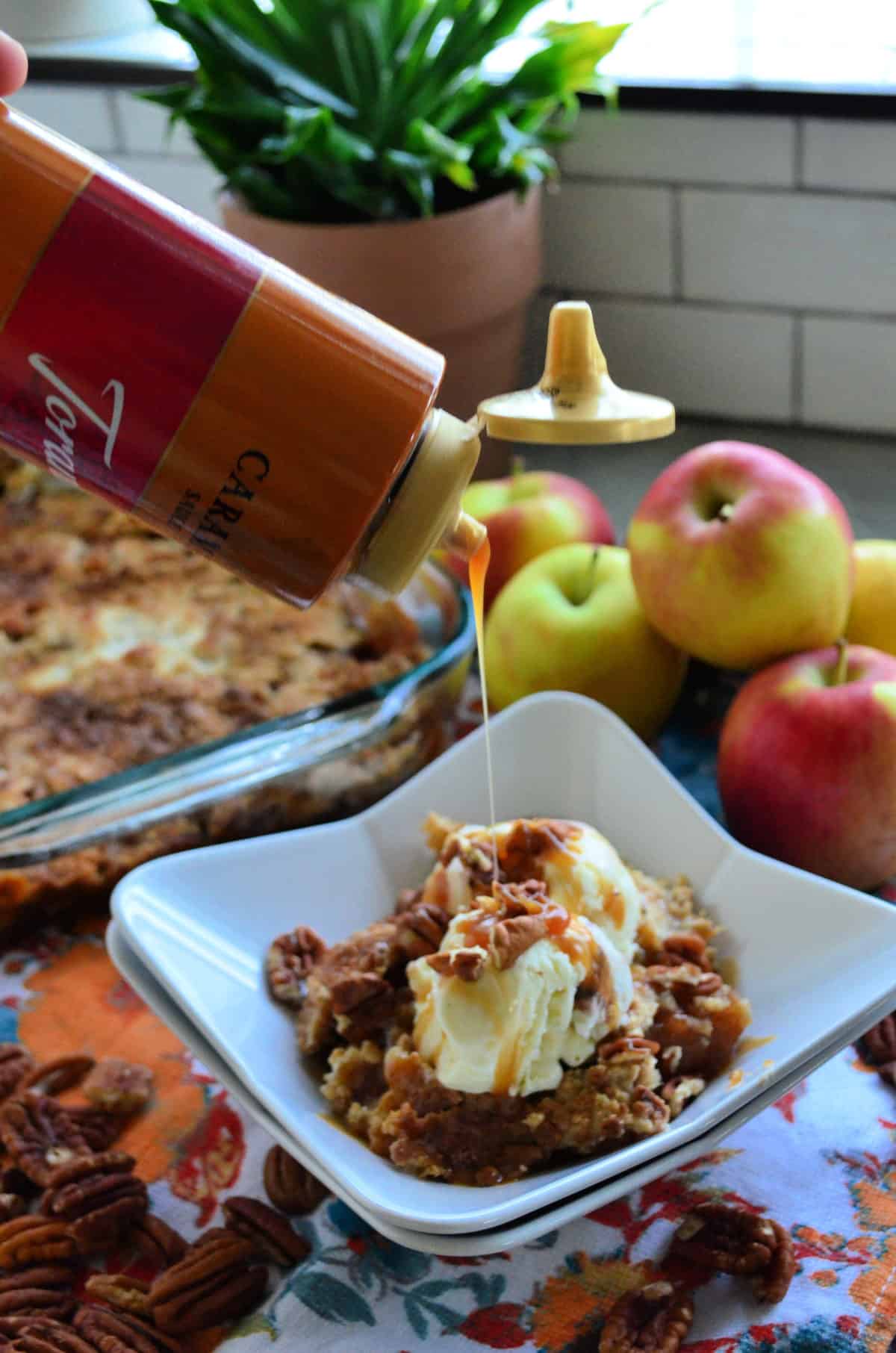 caramel being drizzled over vanilla ice cream on apple dump cake in square dish.