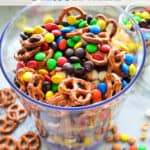 Glass of M&Ms, pretzels, popcorn, and peanuts with pinterest title text.
