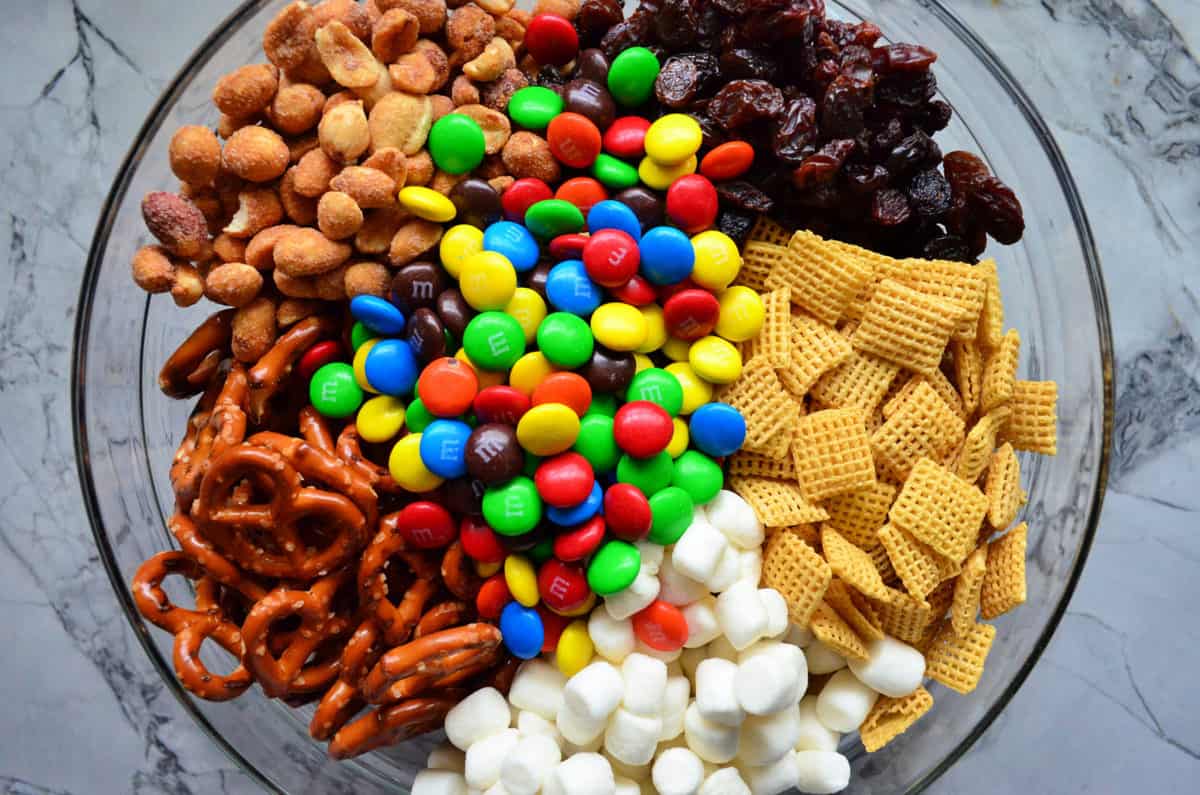 top view glass bowl with chex, mini marshmallows, pretzels m&ms, peanuts, and raisins.