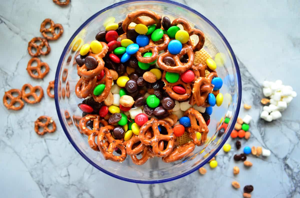 top view glass bowl with chex, mini marshmallows, pretzels m&ms, peanuts, and raisins.