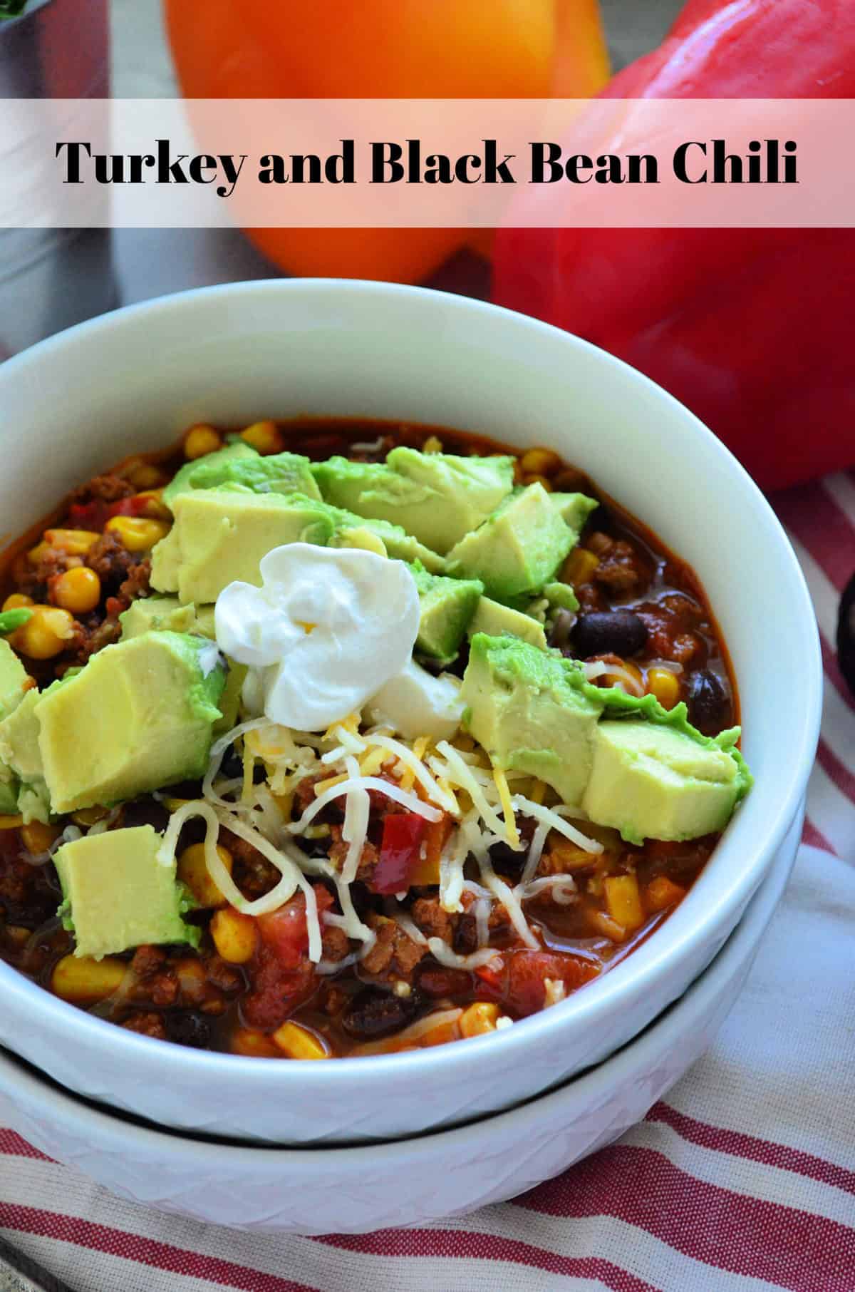 closeup bowl of chili with beans, meat, tomatoes, corn, avocado and shredded cheese with title text.