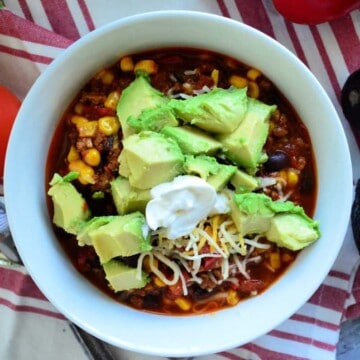 Top view of chili in bowl topped with sour cream, shredded cheese, avocado.