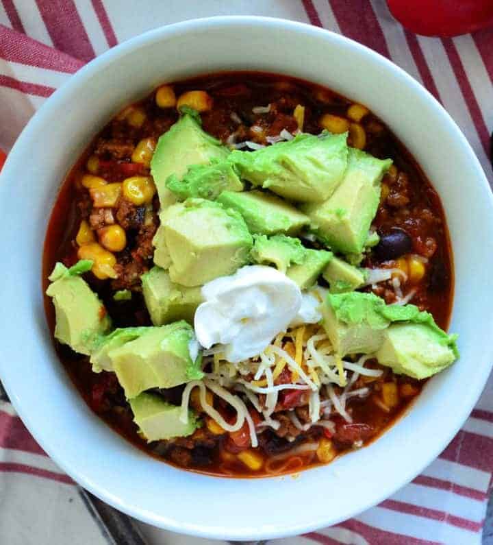 Top view of chili in bowl topped with sour cream, shredded cheese, avocado.