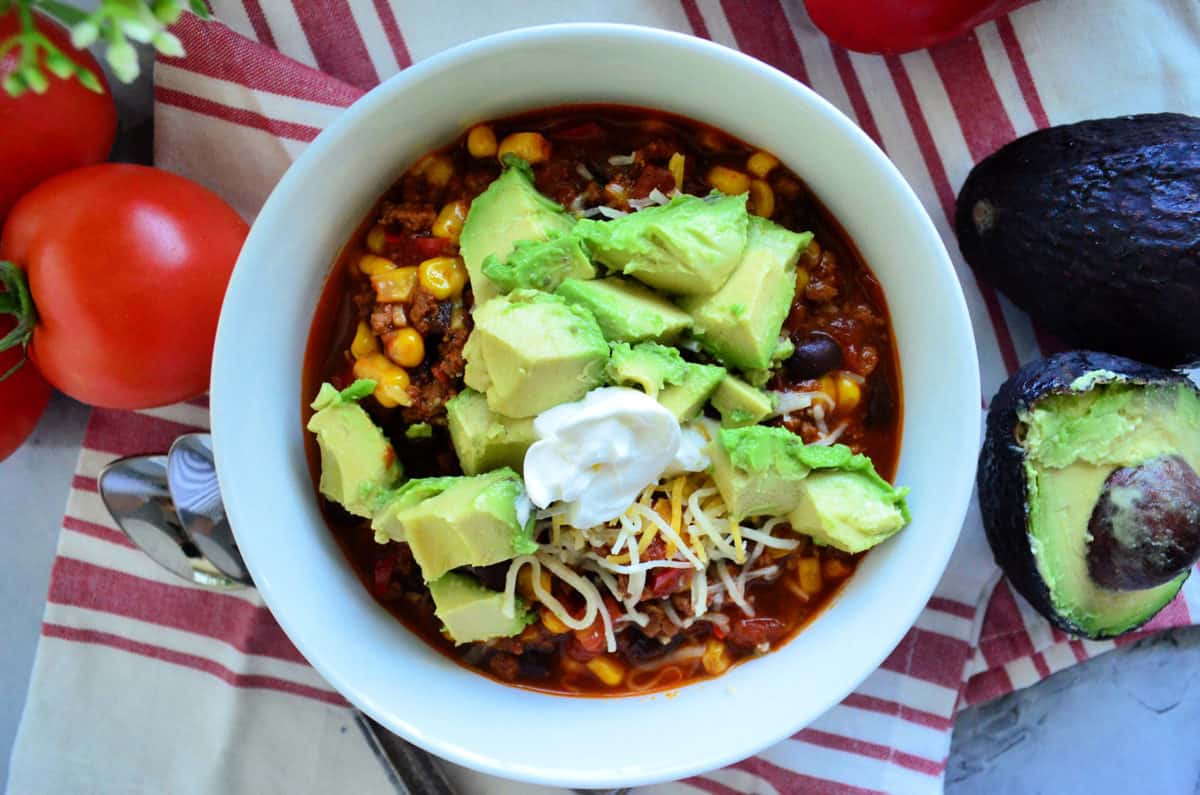 Top view of chili in bowl topped with sour cream, shredded cheese, avocado.