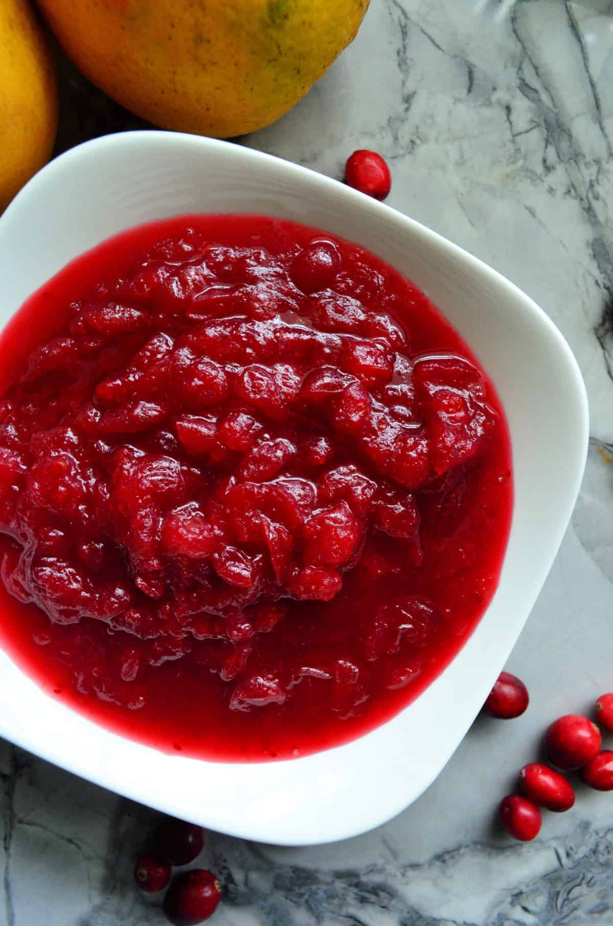 Closeup top view of chunky red cranberry sauce in white bowl on countertop with fresh cranberries.