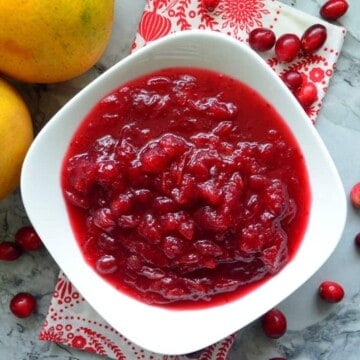 Top view of white bowl filled with homemade cranberry sauce next to oranges.