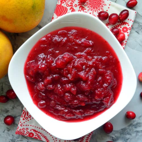 Top view of white bowl filled with homemade cranberry sauce next to oranges.