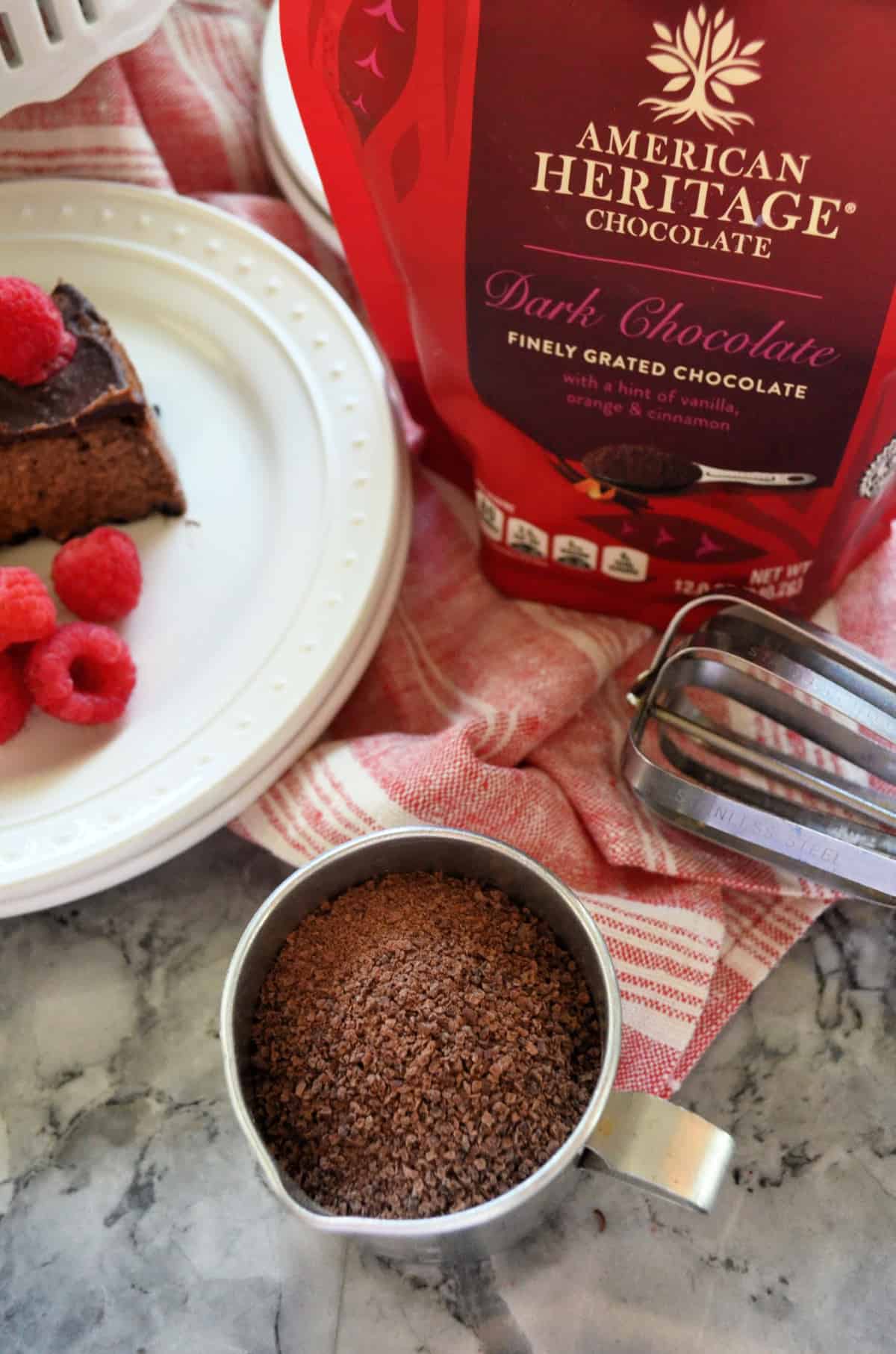 closeup american heritage chocolate package next to whisk and half of plate of cheesecake.