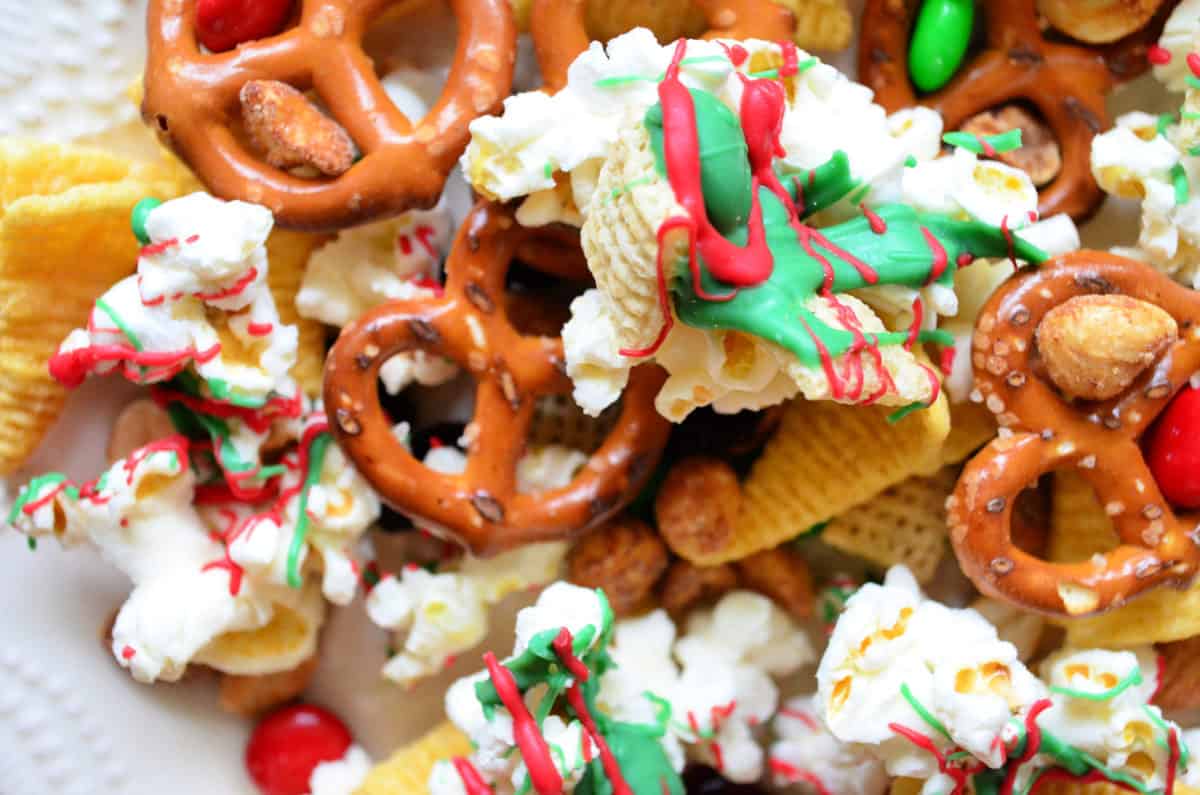 closeup of chex, pretzels, popcorn, nuts, and m&ms drizzled with red and green chocolate.