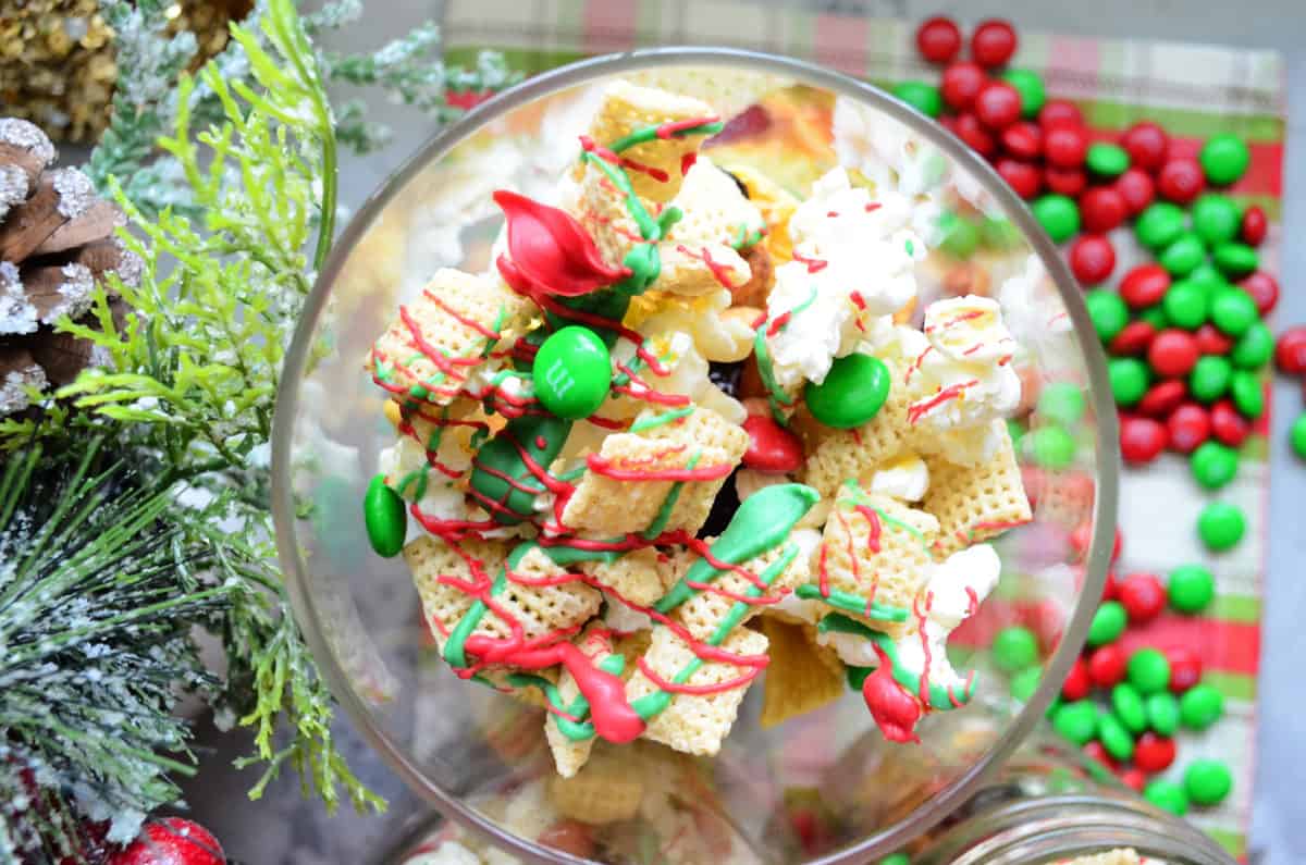 Top view of chex, red and green m&ms, and popcorn drizzled with red and green chocolate in bowl.