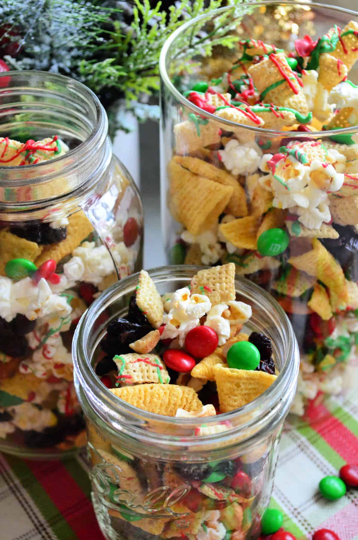 3 class containers of red and green chocolate drizzled check mix, popcorn, and m&ms.