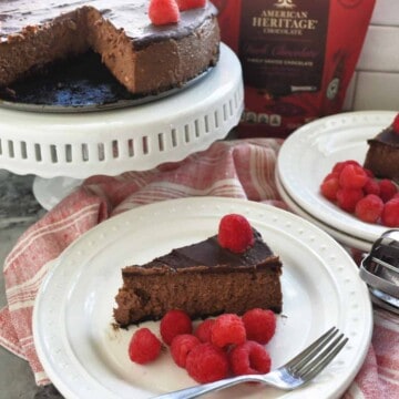 Slice of plated Dark Chocolate Raspberry Cheesecake in front of remaining cheesecake and bag of chocolate.