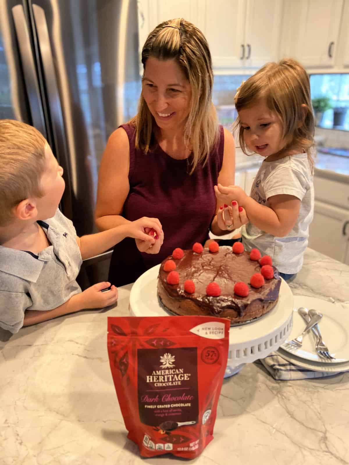 mother and son smile at eachother over cheesecake while daughter sits next to cake smiling at it.