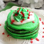 Stack of green pancakes with vanilla cream and green whipped cream and heart sprinkles.