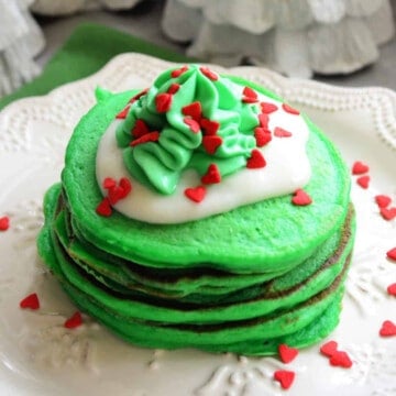 Stack of green pancakes with vanilla cream and green whipped cream and heart sprinkles.