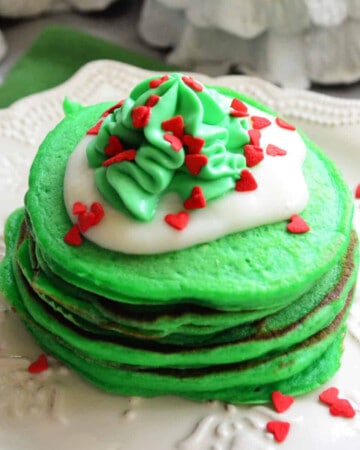 Stack of green pancakes with vanilla cream and green whipped cream and heart sprinkles.