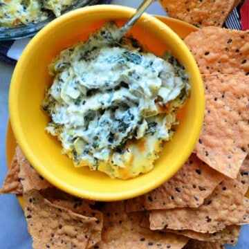 Spinach Artichoke Dip inn yellow bowl with spoon served with chips on the side.