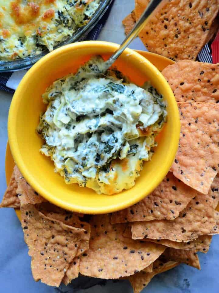 Spinach Artichoke Dip inn yellow bowl with spoon served with chips on the side.