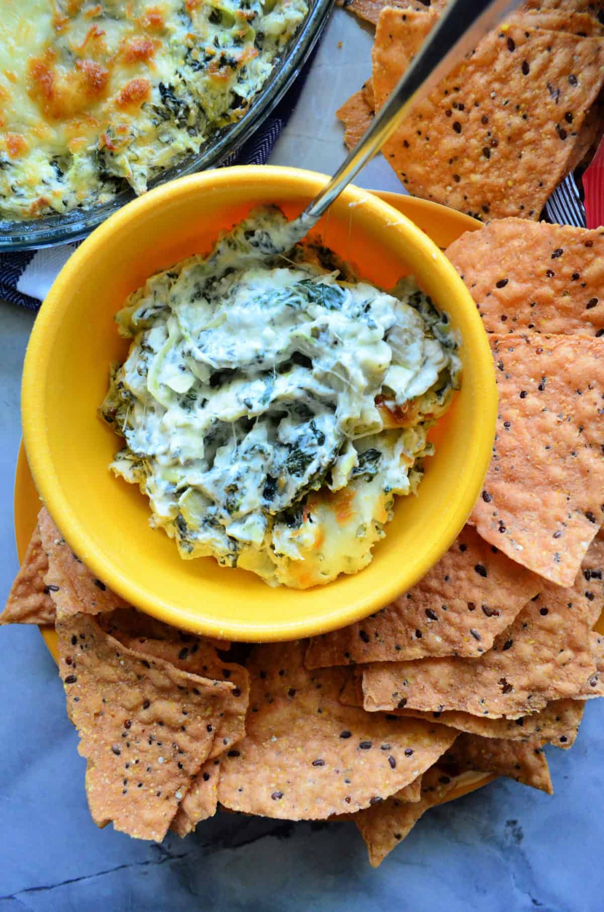 Spinach Artichoke Dip inn yellow bowl with spoon served with chips on the side.