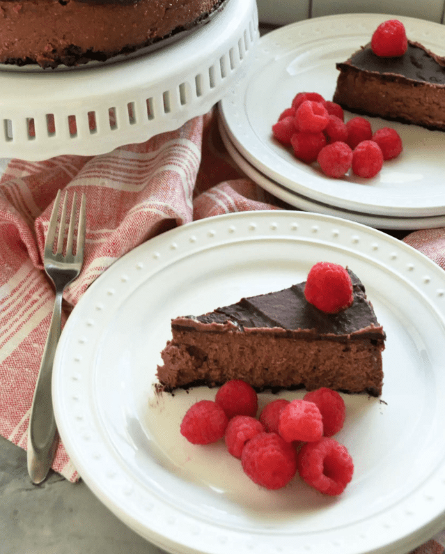 2 Plated slices of dark chocolate cheese cake garnished with fresh raspberries.