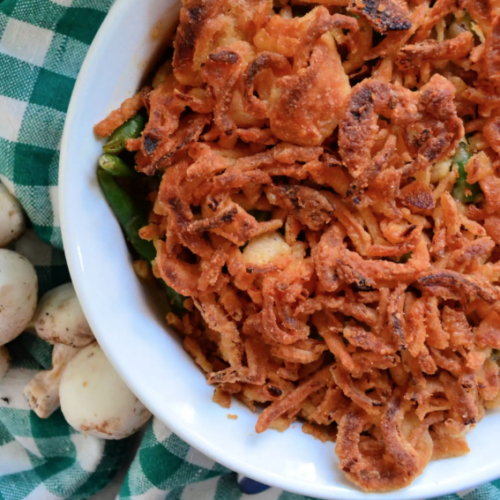 Plated Green bean casserole topped with french fried onions on green checkered tablecloth.