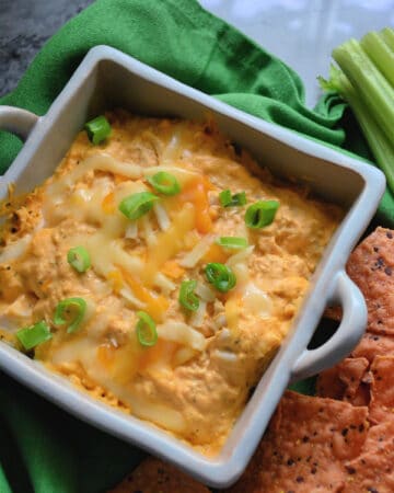 Buffalo chicken dip in a ceramic baking dish served with chips and celery.