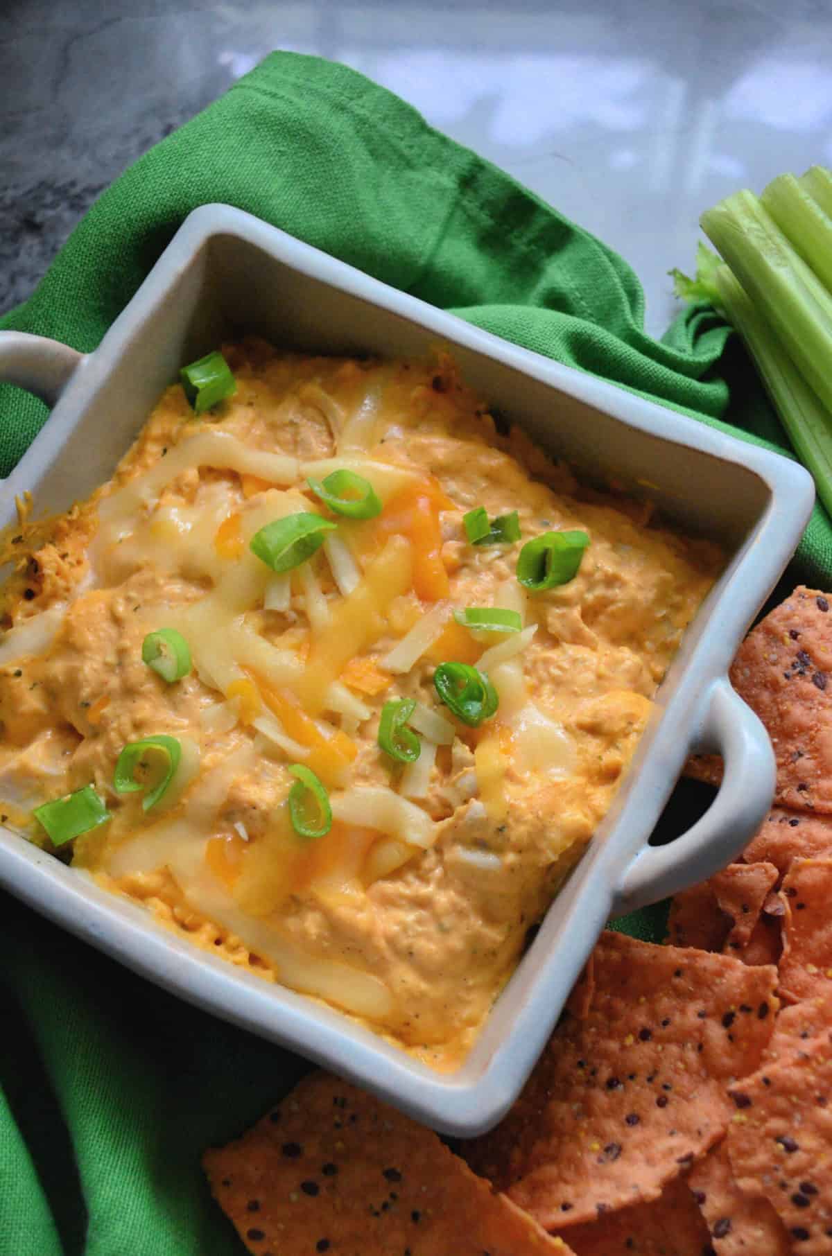 Buffalo chicken dip in a ceramic baking dish served with chips and celery.