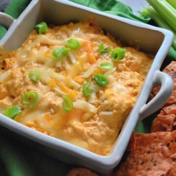 Buffalo chicken dip in a ceramic baking dish garnished with green onion and melted cheddar.