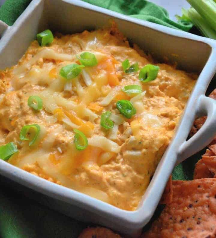 Buffalo chicken dip in a ceramic baking dish garnished with green onion and melted cheddar.