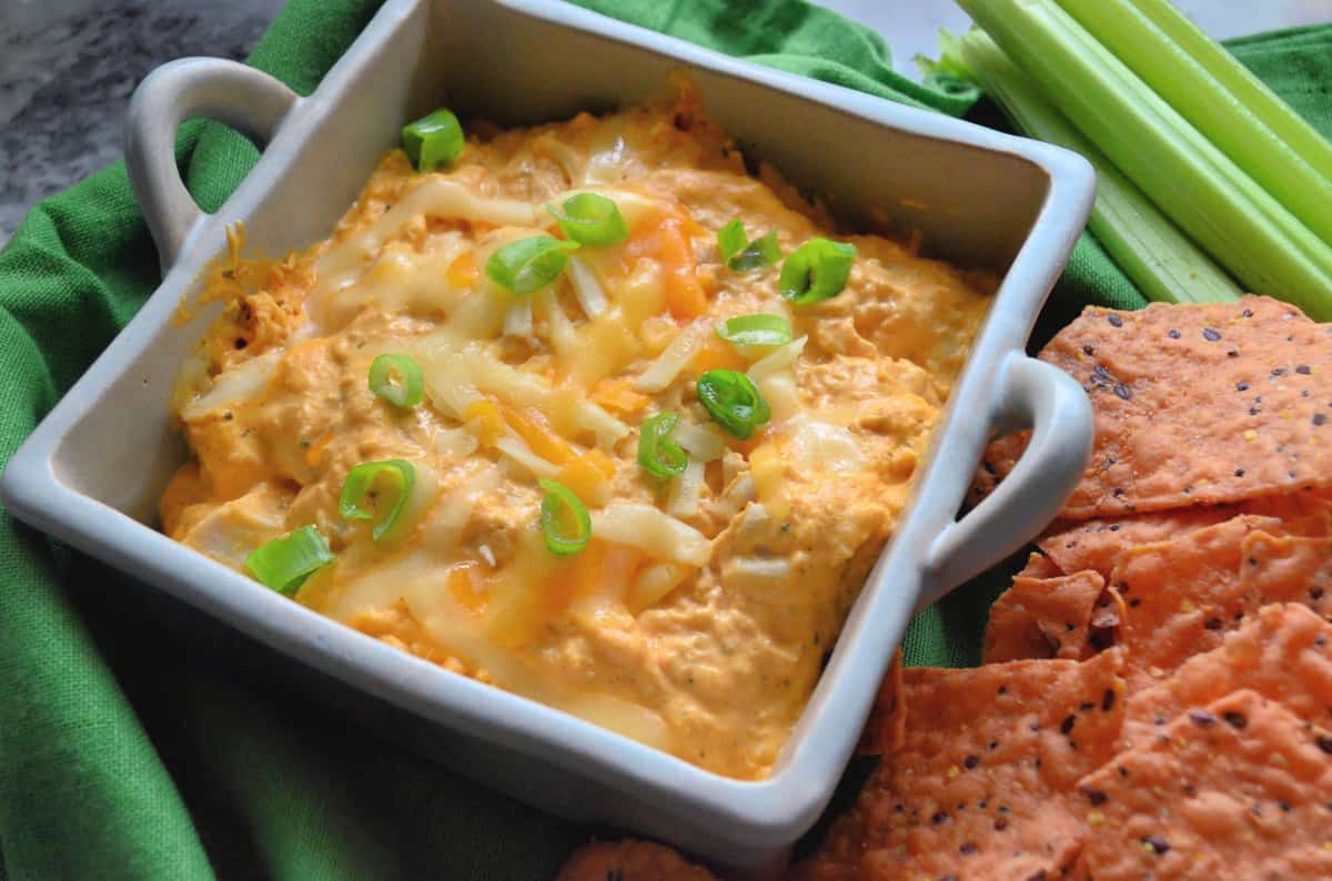 orange dip topped with melted cheese and chives in square dish served with celery and chips.