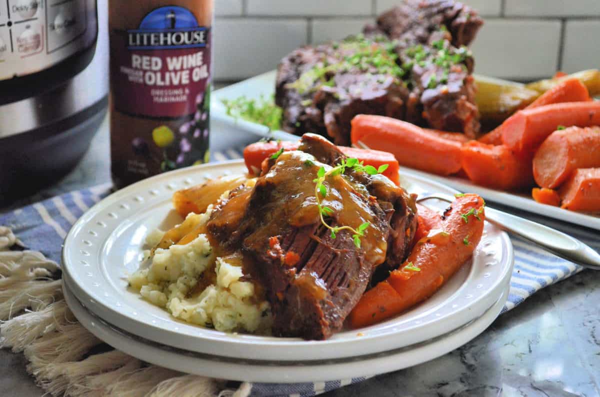 plated pot roast and carrots plated over mashed potatoes and topped with herb garnish and gravy.