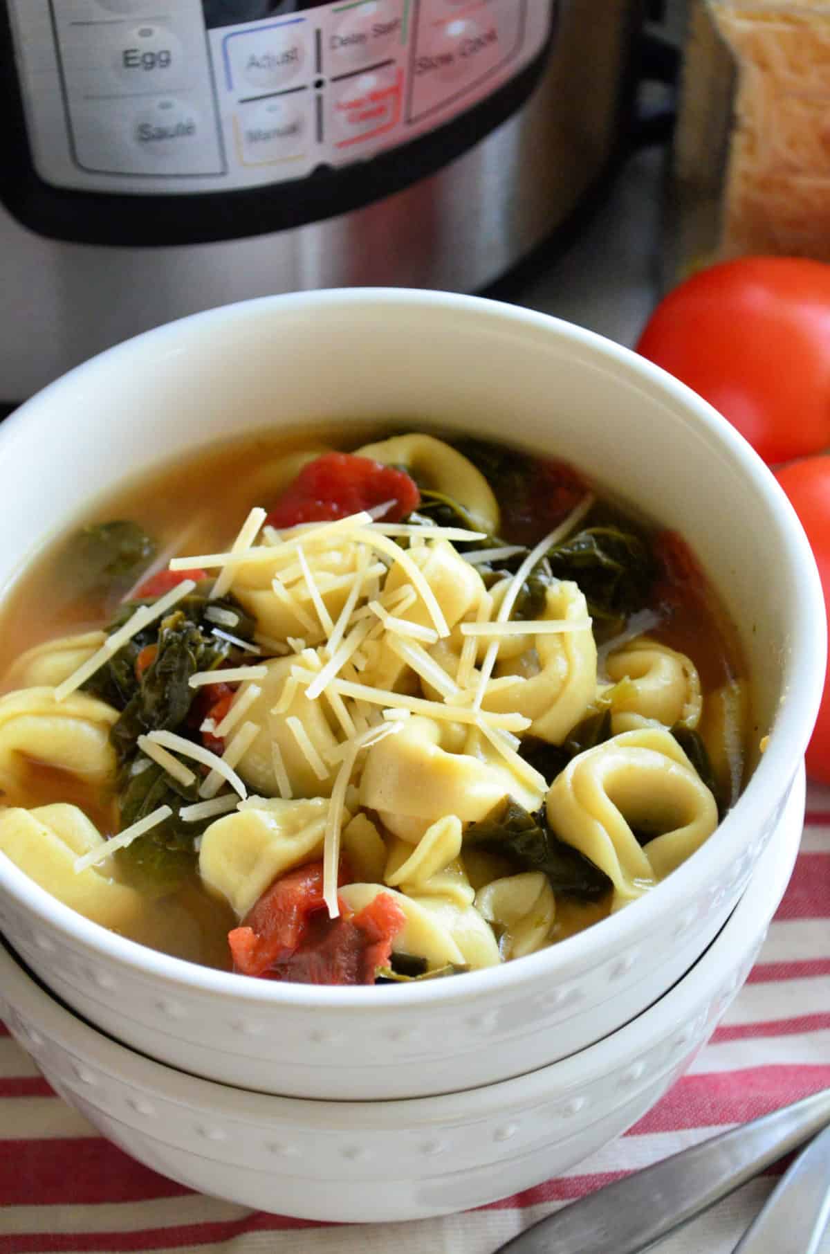 closeup top view of bowl of tortellini soup with spinach, tomato, and shredded cheese.