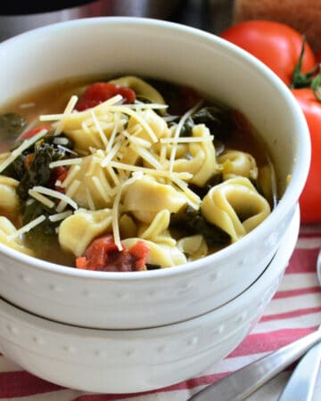 Two bowls stacked in front of vine ripened tomatoes. Top bowl filled with spinach tortellini soup.