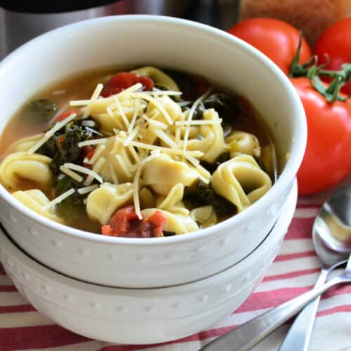 Two bowls stacked in front of vine ripened tomatoes. Top bowl filled with spinach tortellini soup.