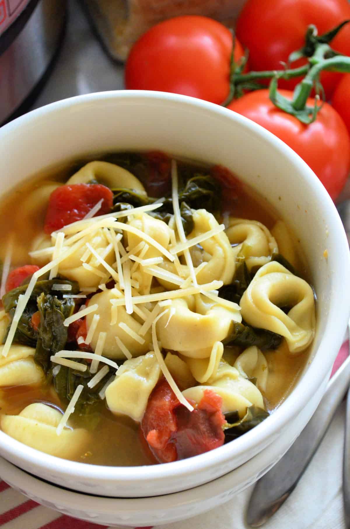 close up top view of bowl filled with broth, tortellinis, tomatoes, spinach, and topped with shredded cheese.