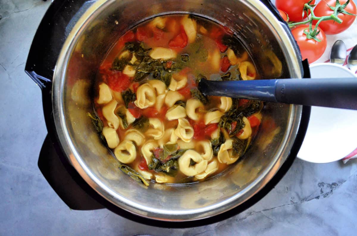 top view of Broth, spinach, tortellini, and tomato in instant pot.