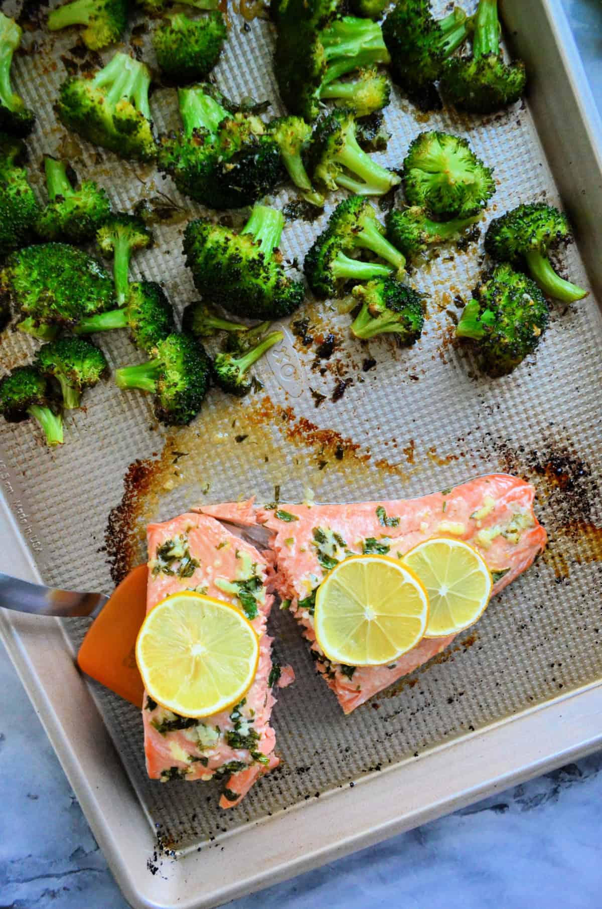 Sheet pan with salmon, lemon slices and broccoli.
