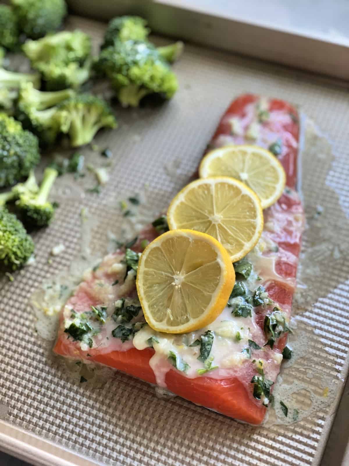 sheet pan with salmon topped with white herb sauce and lemon wheels prior to cooking.