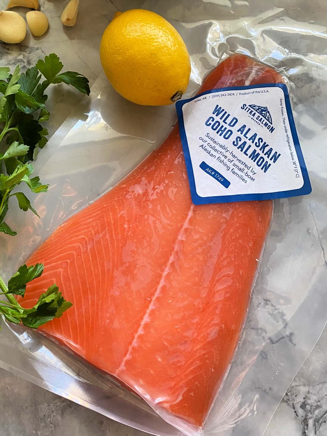 top view of packaged wild alaskan coho salmon on countertop with parsley and whole lemon.