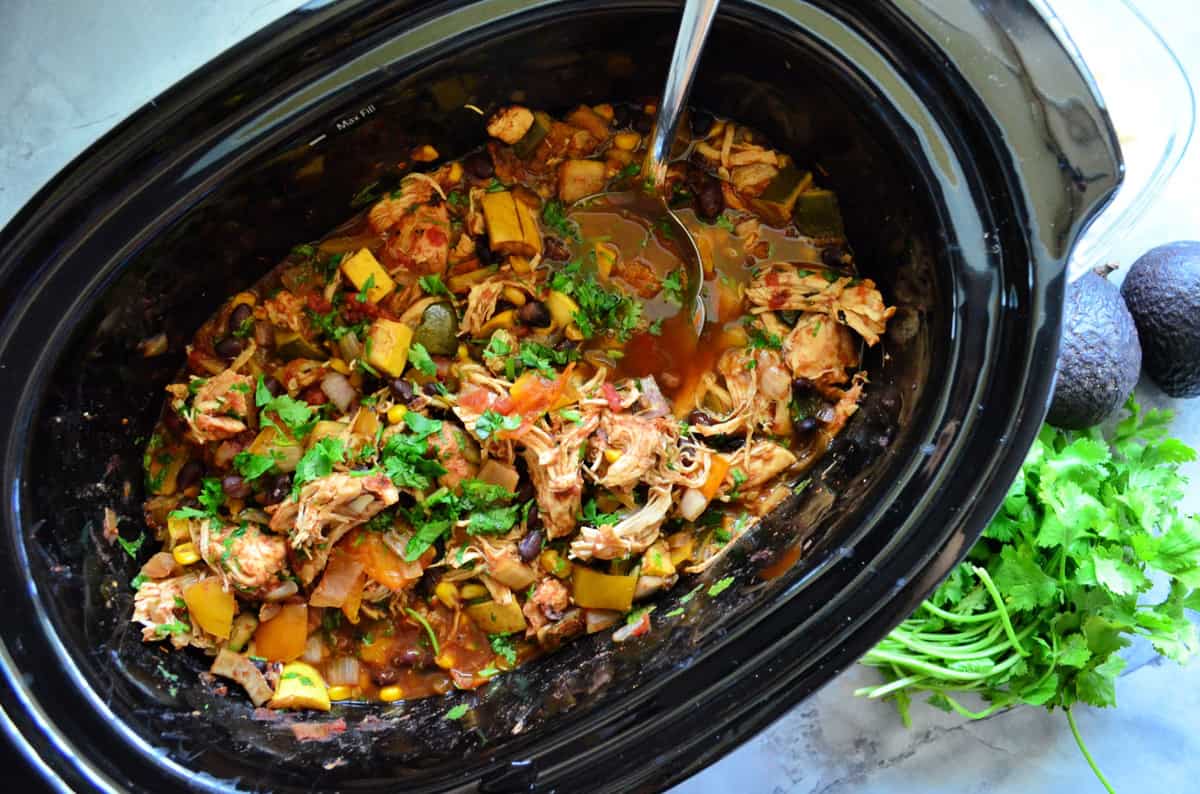 Top view of a black oval slow cooker with shredded chicken and veggies.