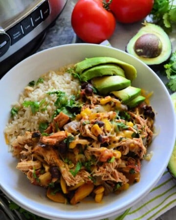 Bowl of rice with chicken, black beans, avocado and ingredients artistically next to bowl.