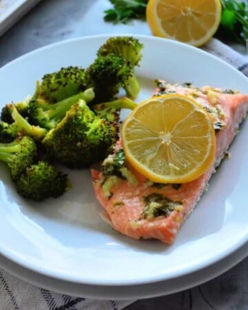 Plated Lemon Butter Garlic Salmon with Broccoli. Lemon and Parsley garnish in background off plate.