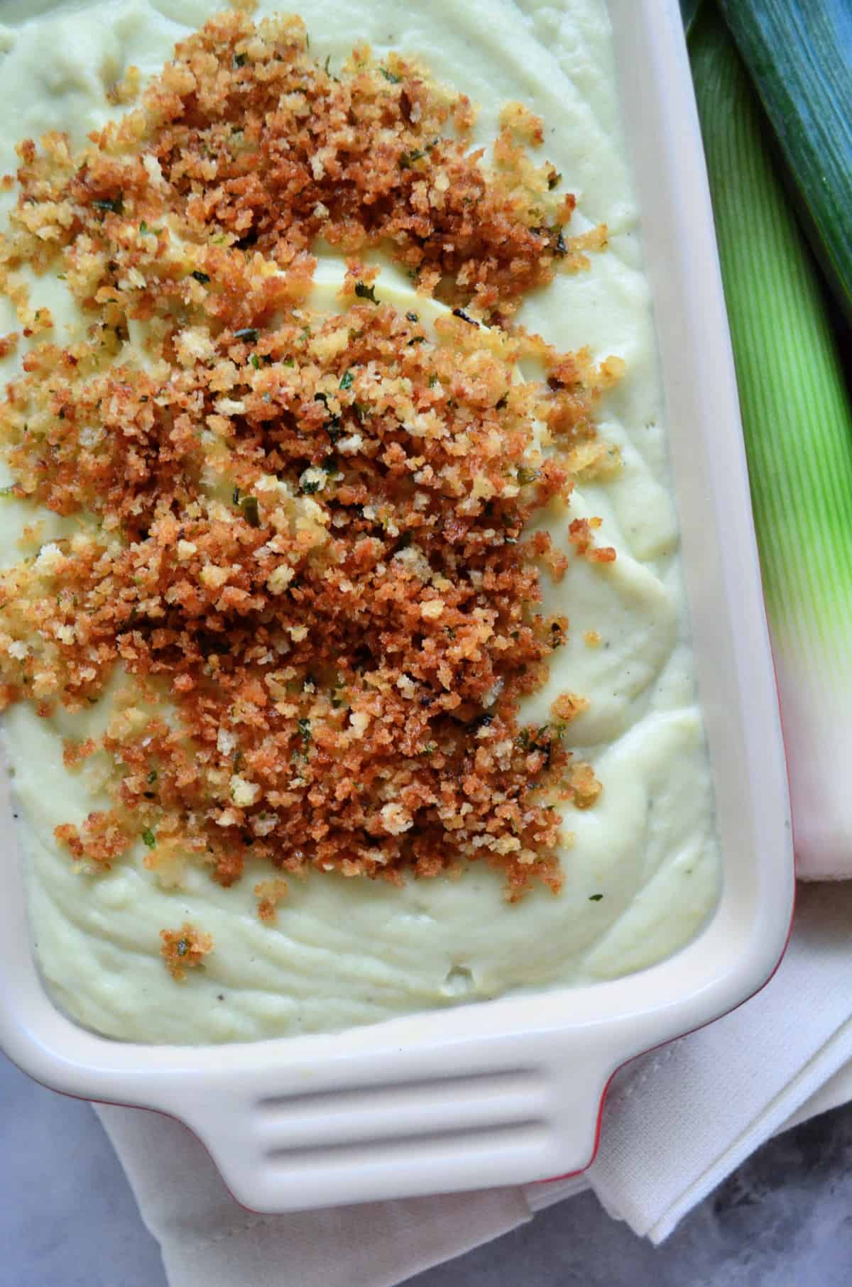 close up top view of white puree topped with panko bread crumbs next to leek.