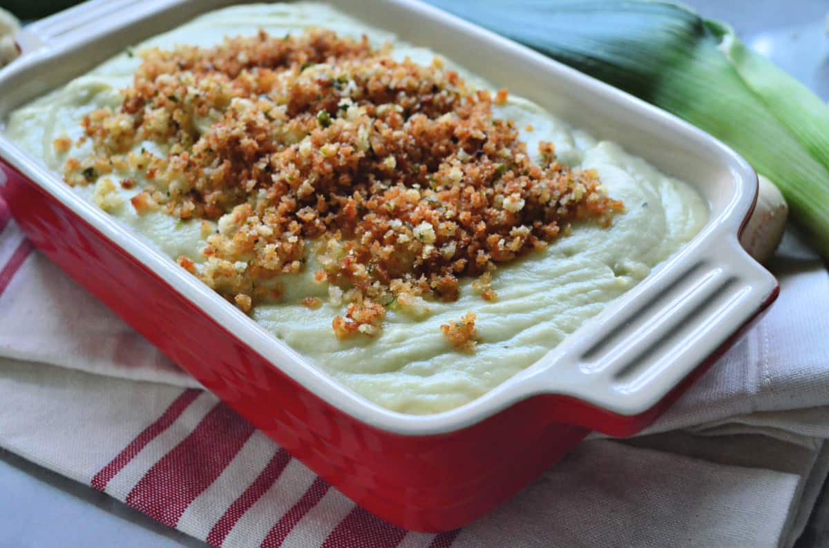A red casserole dish with Cauliflower-Leek Puree in it topped with panko bread crumbs.